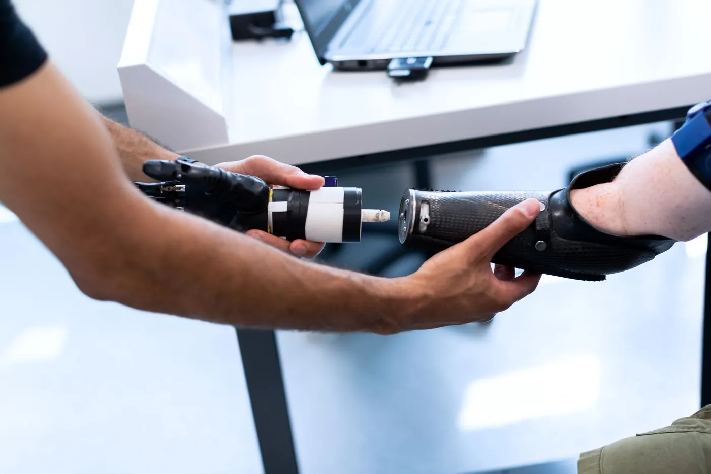 Two people fitting a black prosthetic arm at a desk