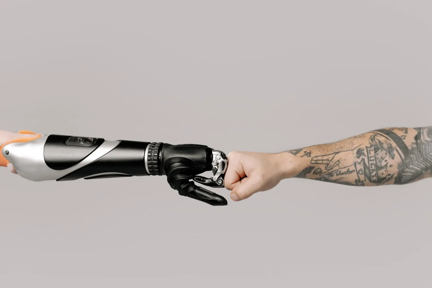 A black and white robotic forearm meeting a tattooed human fist