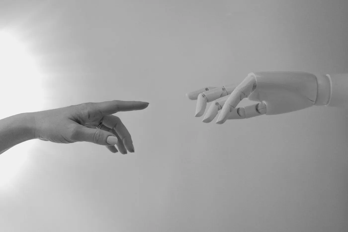 A grey robotic hand and a human hand reaching toward each other, in black and white