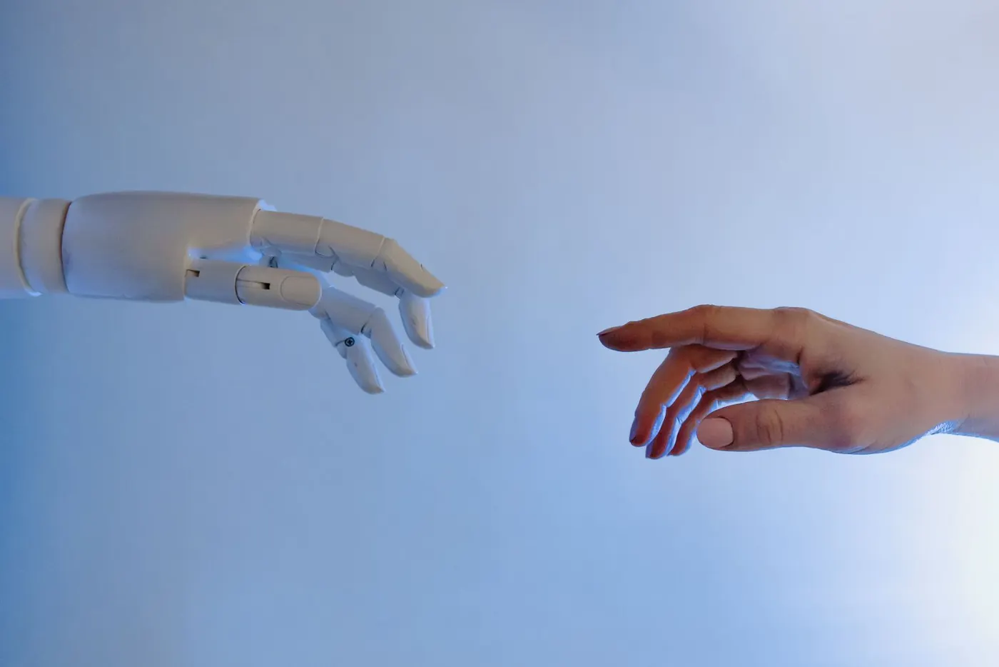 A pale robotic hand and a human hand reaching across a blue gradient