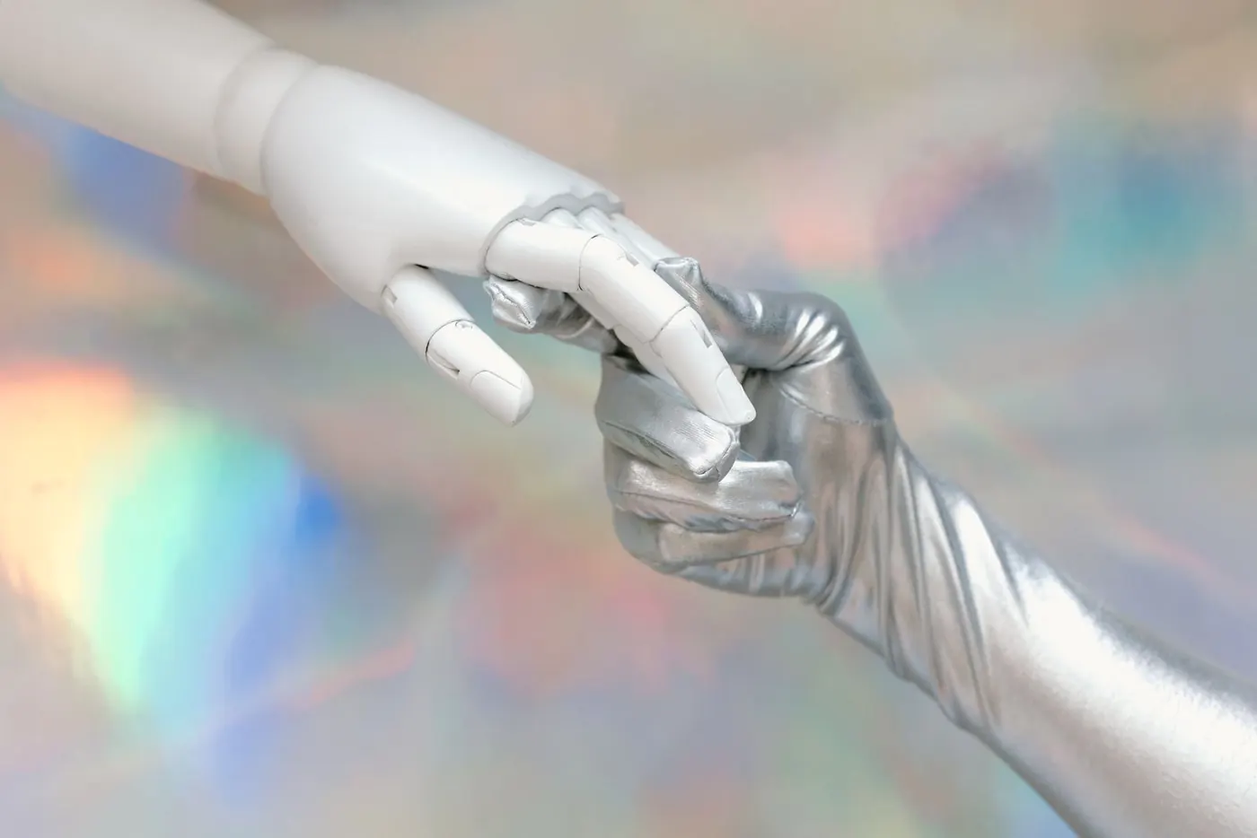 A hand in a silver glove holding a white robotic hand against a holographic backdrop